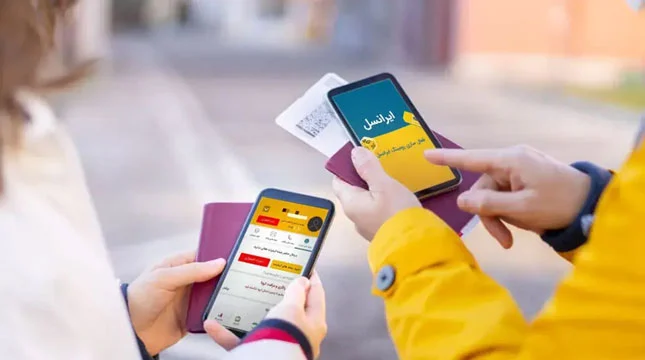 دو نفر در حال بررسی اپلیکیشن ایرانسل روی گوشی‌های هوشمند، یکی از آن‌ها در حال استفاده از خدمات رومینگ و پرداخت قبض هنگام سفر با پاسپورت و بلیت در دست؛ نماد پرداخت قبض ایرانسل از خارج کشور در حین سفر